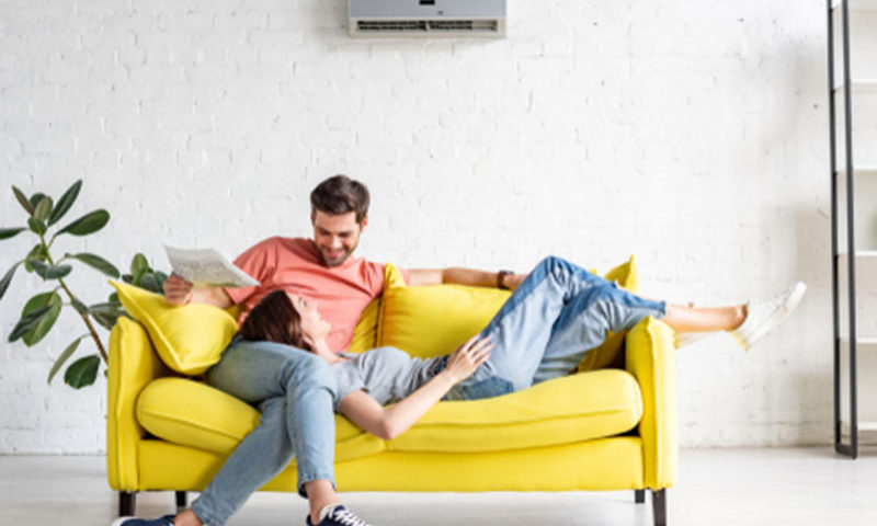 Couple on a couch staying cool with a ductless air conditioner unit on wall.