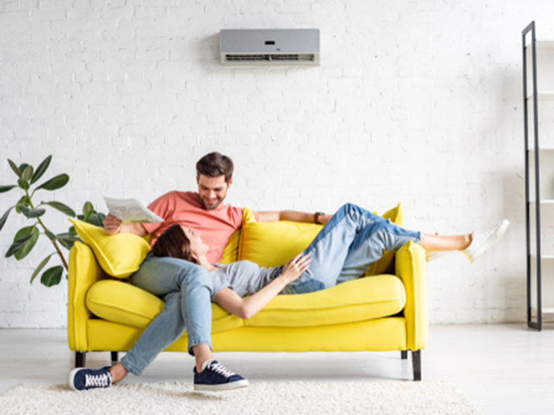 Couple on a couch staying cool with a ductless air conditioner unit on wall.