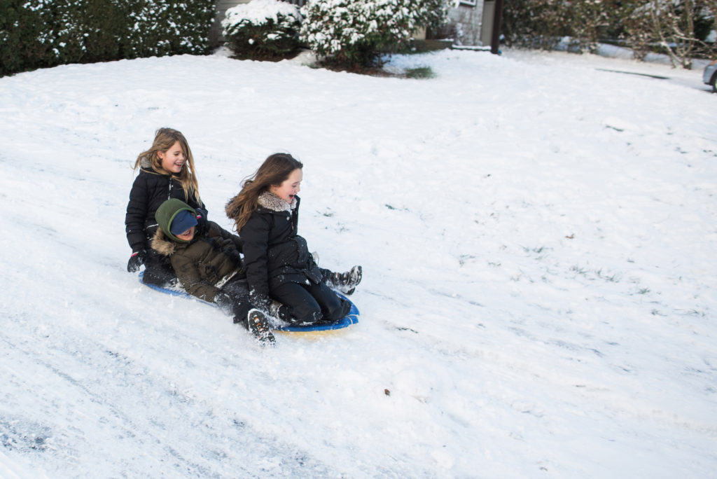 Happy kids sledding down a hill in winter.